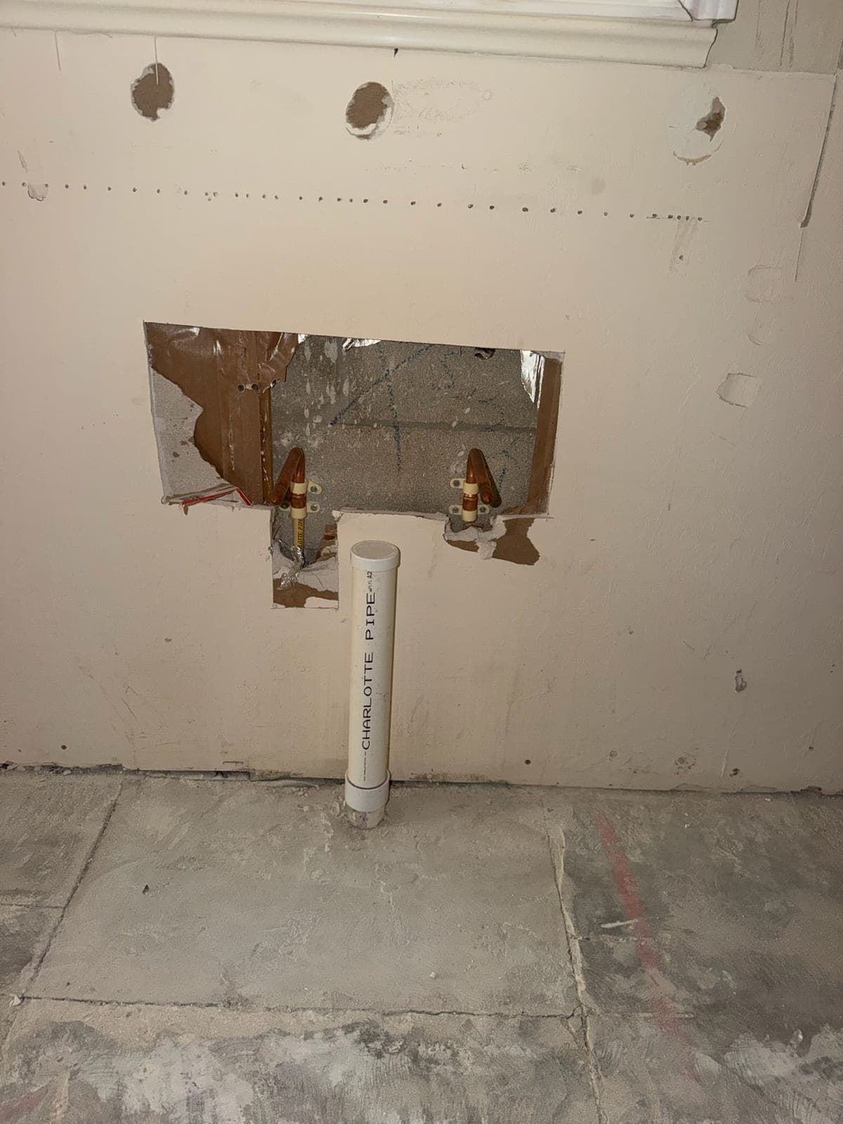 Copper supply stub-outs and a PVC waste riser exposed in an opened wall section
