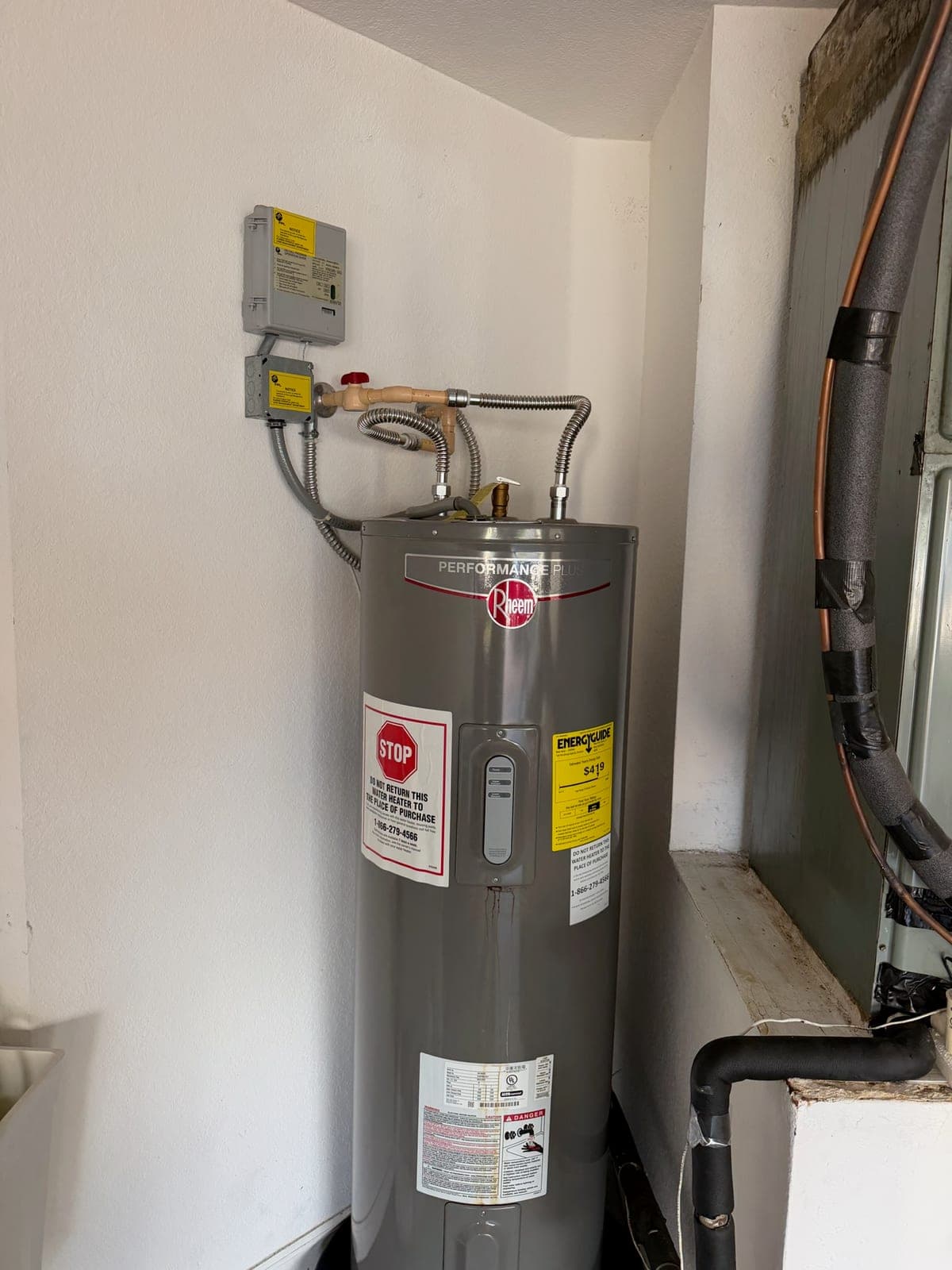 Newly installed Rheem electric water heater with flexible supply connectors and a disconnect box