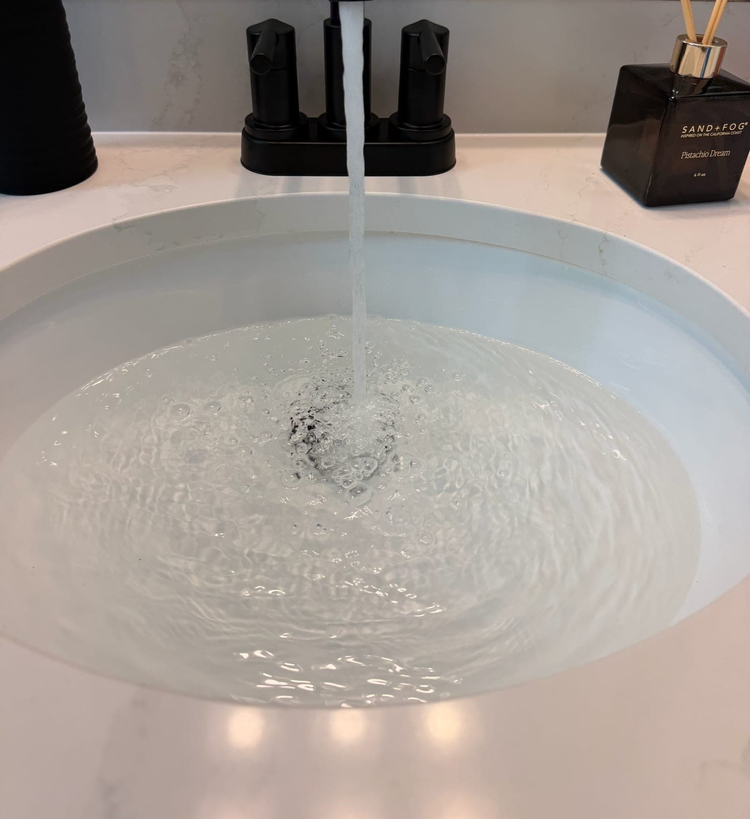 New matte black lavatory faucet running clear water into a white vessel sink