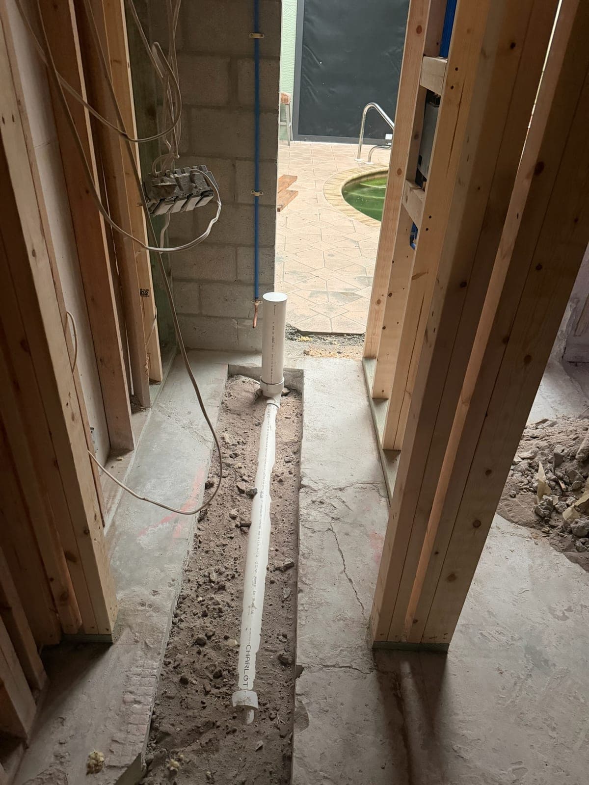 New PVC drain line and riser set in a trench cut through a concrete slab
