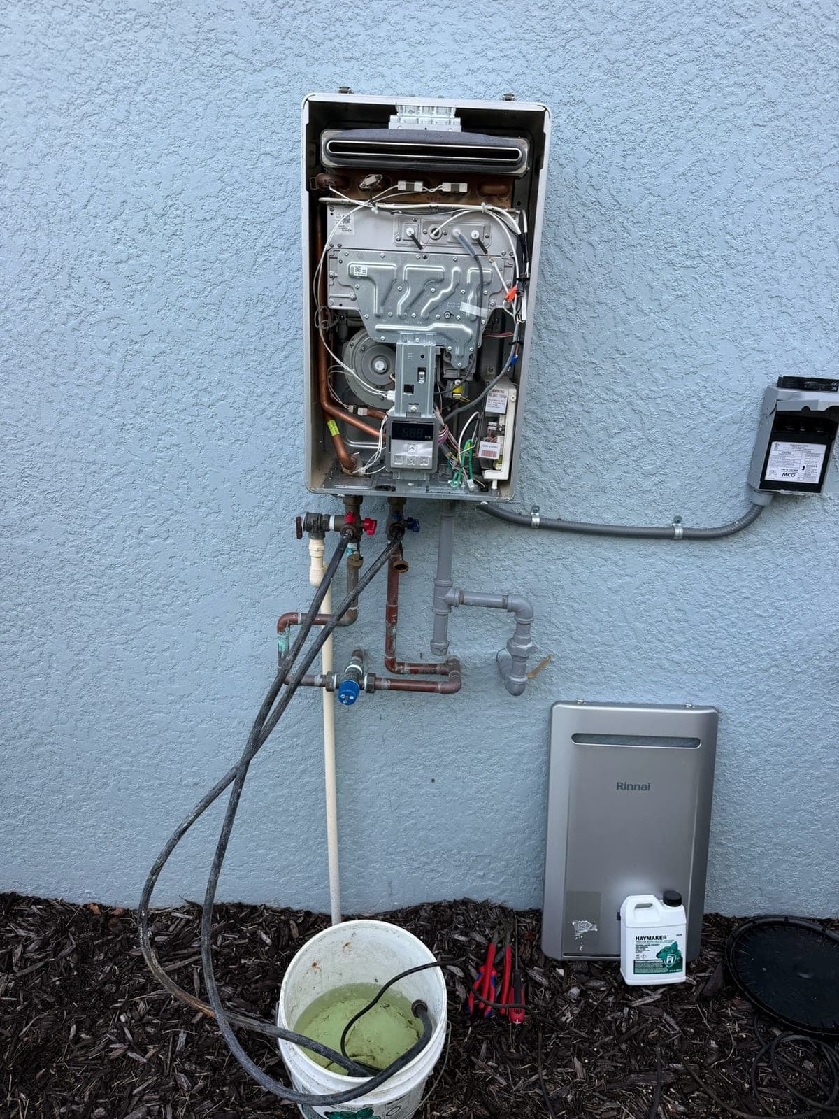 Wall-mounted Rinnai tankless water heater opened up with descaling pump and hoses connected