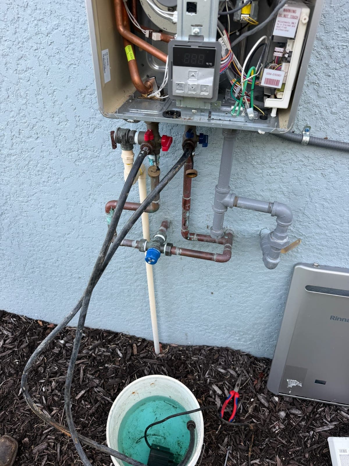Rinnai tankless water heater with its cover removed showing the heat exchanger, control board and gas piping