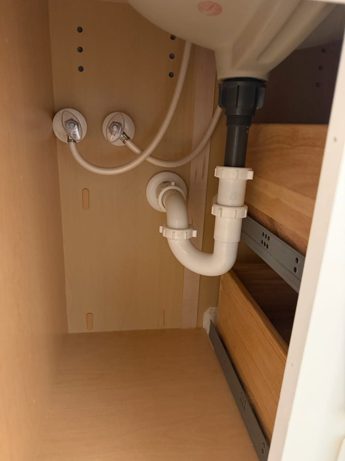 Under-sink trap assembly and braided supply lines routed neatly inside a cabinet